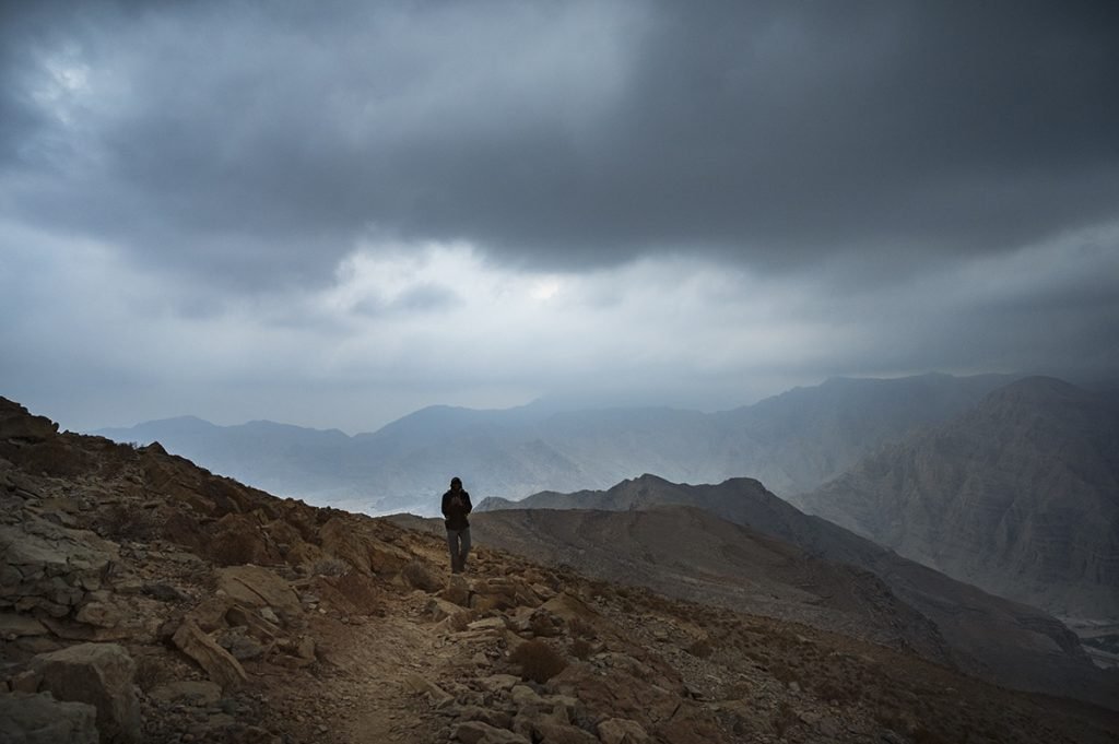 a man walking on the mountain trail in the uae on the cloudy evening after the sunset
