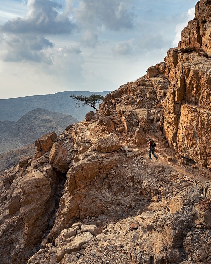 A man hiking on mountain trail in the UAE with a backpack on a cloudy day