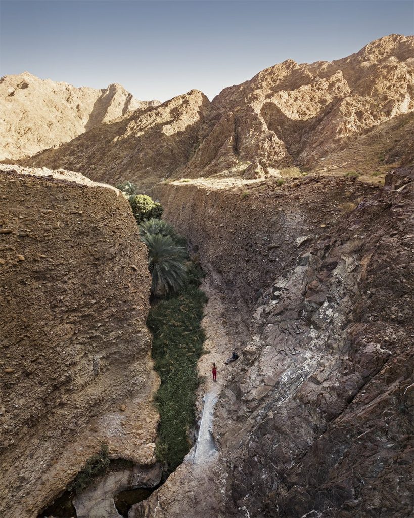 a couple in the ravine with green farm in the middle of steep banks