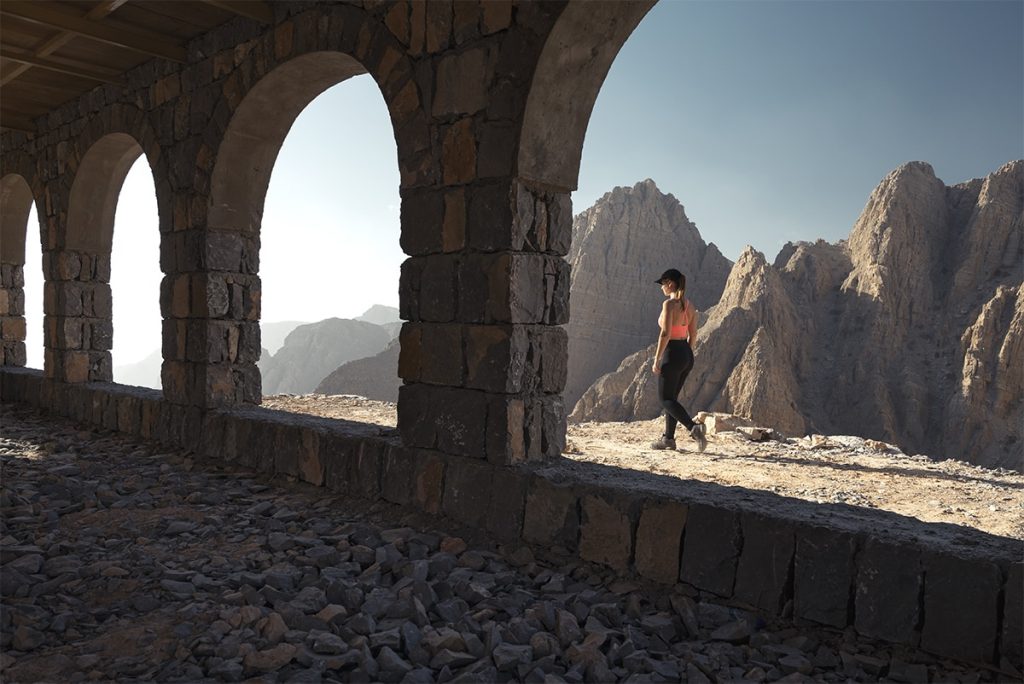 woman walking pass the building with arches with a mountain view in the backdrop