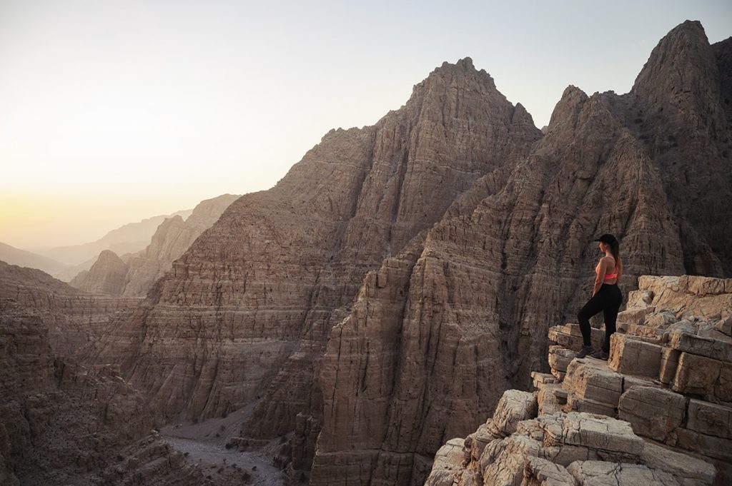 A woman standing at the edge of the mountain during the sunset