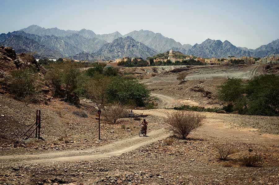 pakistani man on a bycicle riding through hatta mountain with town views in the backdrop