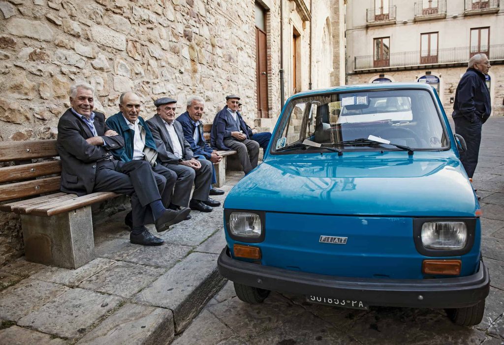 sicily travel tips-old men sitting on the bench next to blue fiat- sicily driving tips