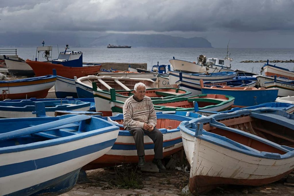 a man sitting on a colorful boat surrounded by many boats in Aspra town in Sicily