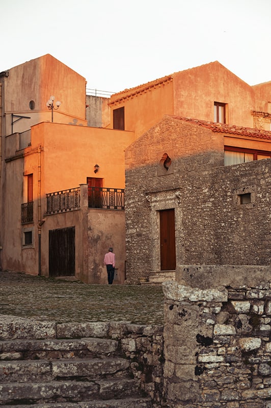 a man in pink shirt walking erice town streets in sicily
