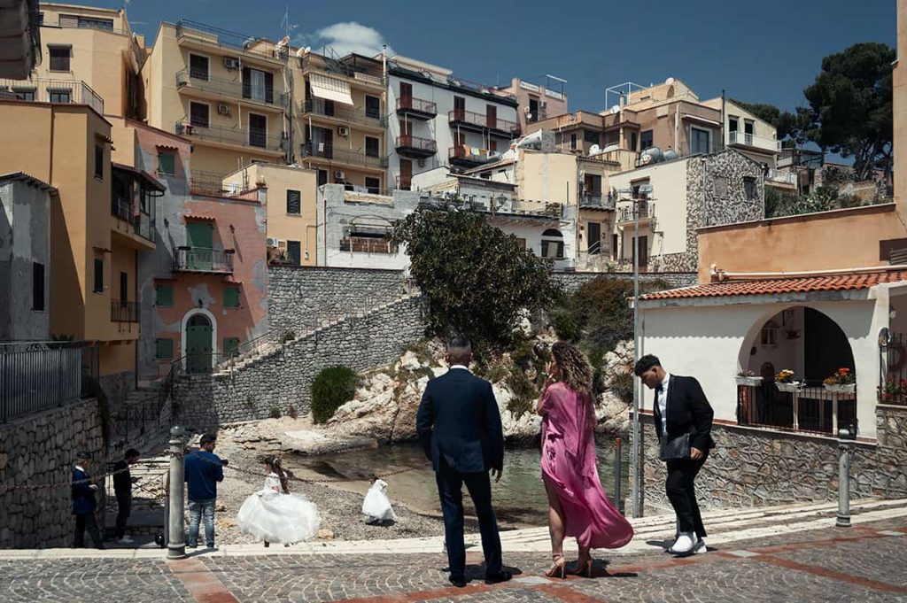 lady in purple dress, men in suits and little girls in white princess dresses on a wedding photoshoot in sant'ellia town in sicily