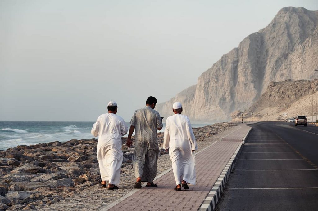 renting a car in oman and tips for driving in oman- road in musandam, 3 omani locals walking on the sidewalk