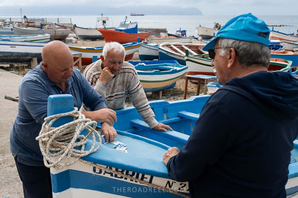 Cheerful local fishermen playing cards in Aspra beach town in Sicily