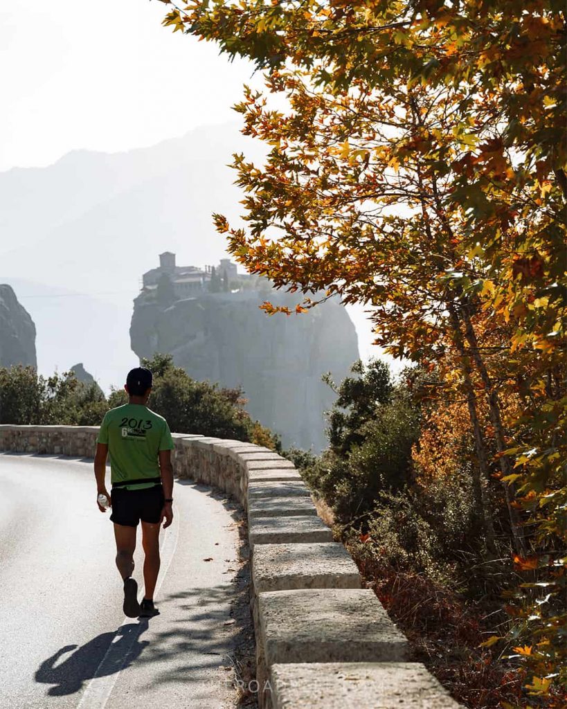 a man walking along the main road in meteroa with holy trinity monastery in the background