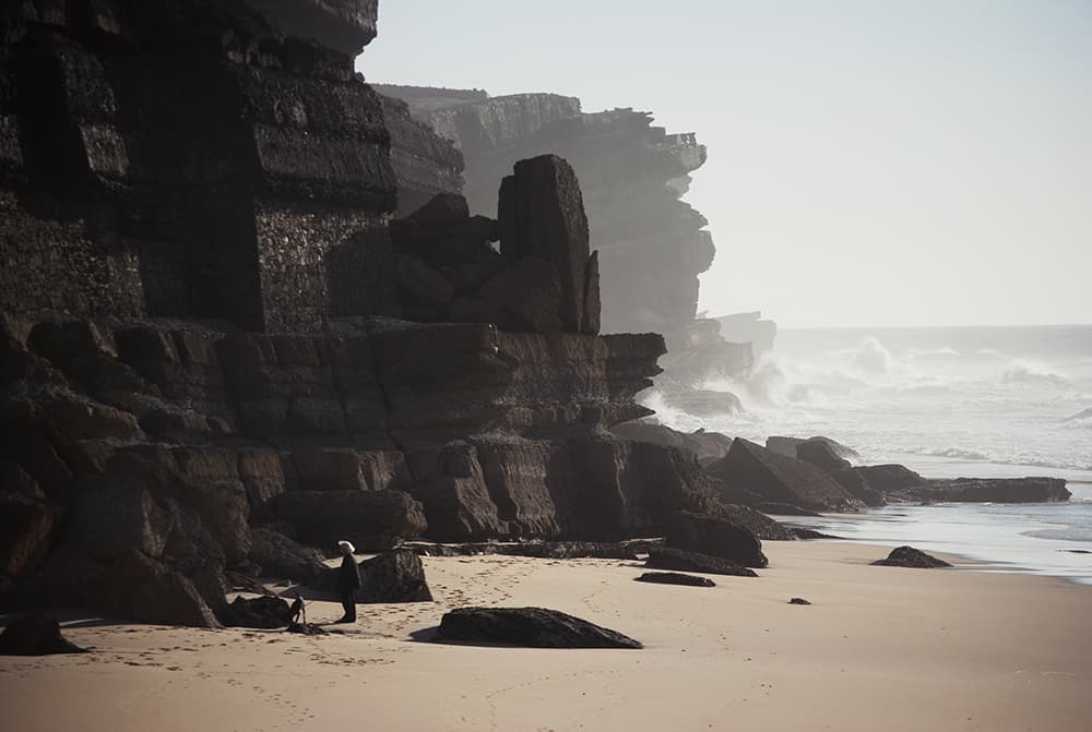 Azenhas do Mar beach, Portugal. A lady walking a dog on the beach with high cliffs