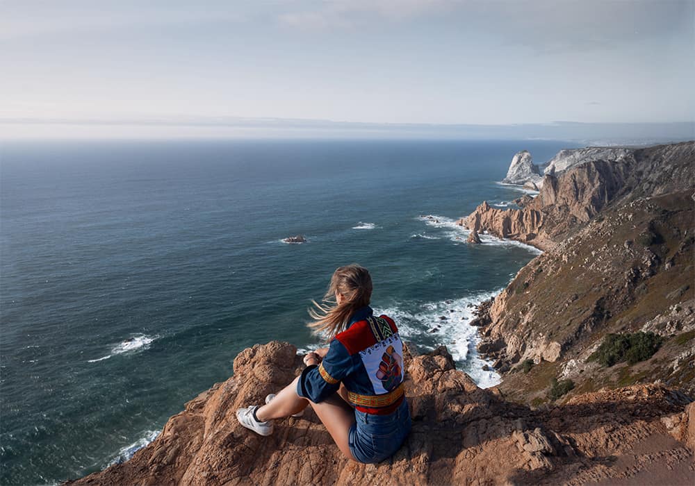 Cabo da Roca- the westernmost point in Europe can be visited by hiking from Azenhas do Mar (you can drive there too). A woman sitting on the cliff in Cabo do Roca Portugal
