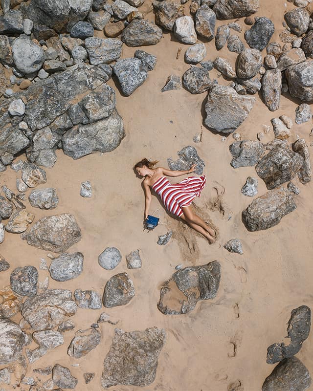 drone photo of a girl laying down on a sandy and rocky beach in Portugal