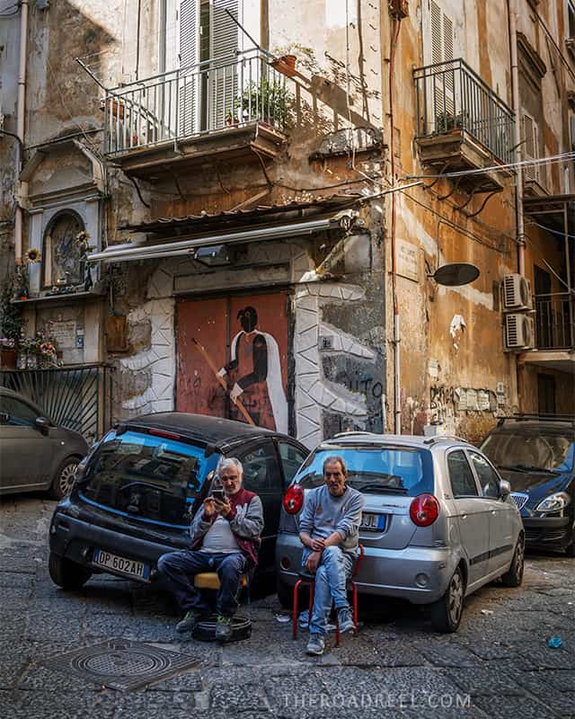 naples streets in quartieri spagnoli two men sitting by the cars and a mural behind them