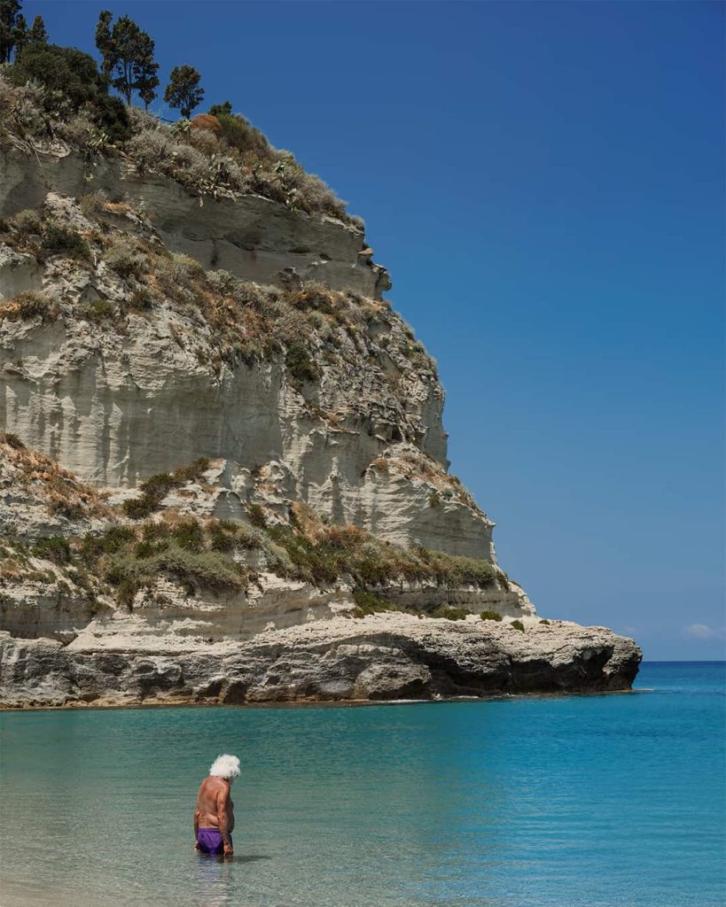 an old man with white long hair entering the water in tropea italy