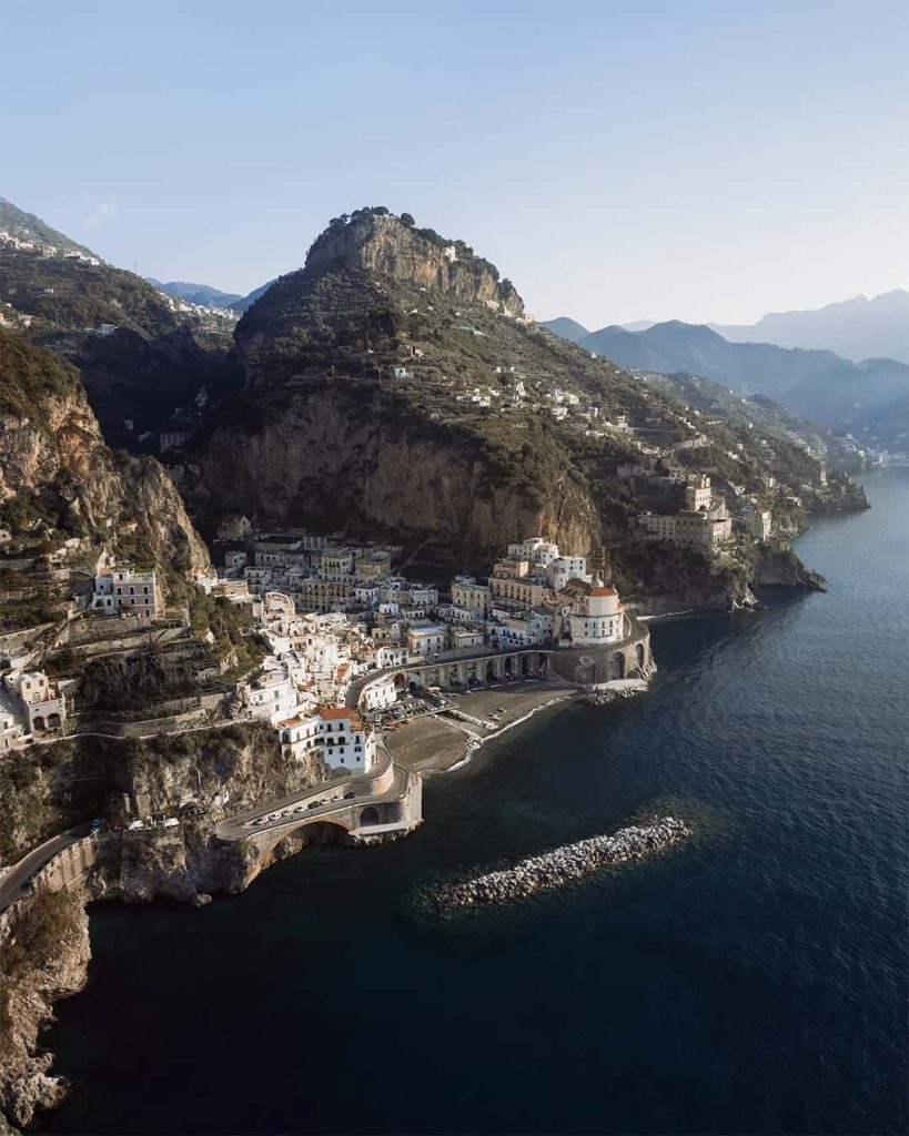 Breathtaking aerial view of Atrani, a tranquil coastal enclave and one of the best towns to visit on the Amalfi Coast, with its distinctive white buildings and the Church of Santa Maria Maddalena, perched between the steep cliffs and the calm azure waters of the Mediterranean.