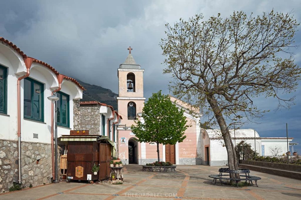 A tranquil square in Nocelle, featuring traditional architecture, a church with a bell tower, and a lone tree, epitomizing the peaceful ambiance of this Amalfi Coast hilltop town.