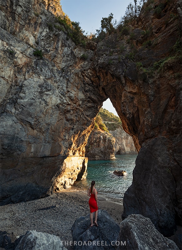 arcomagno beach, arch at sunset and a woman in orange dress standing on the rocks