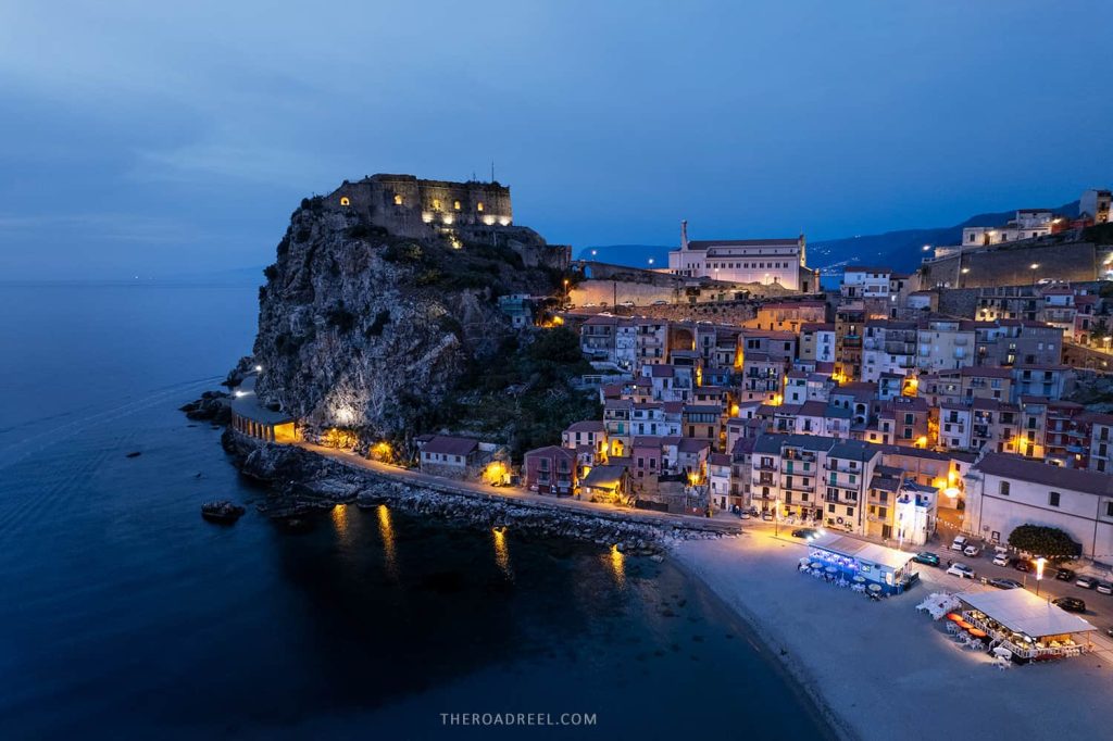 drone image of Scilla, Calabria at dusk. Castelo Rufollo and Marina of Scilla lit up with evening lights