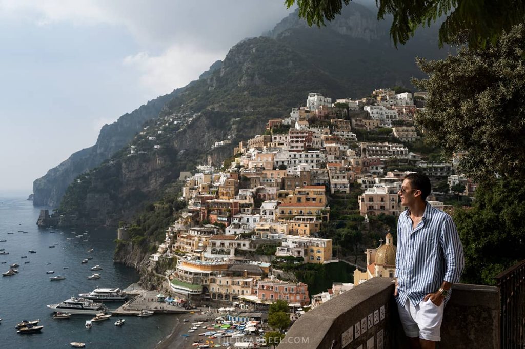 is positano worth visiting? a man in linen stripe shirt posing at a famous viewpoint