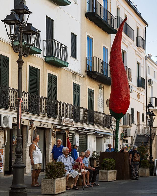 old men sitting on the bench with huge sculpture of peperoncino next to them in diamante town calabria