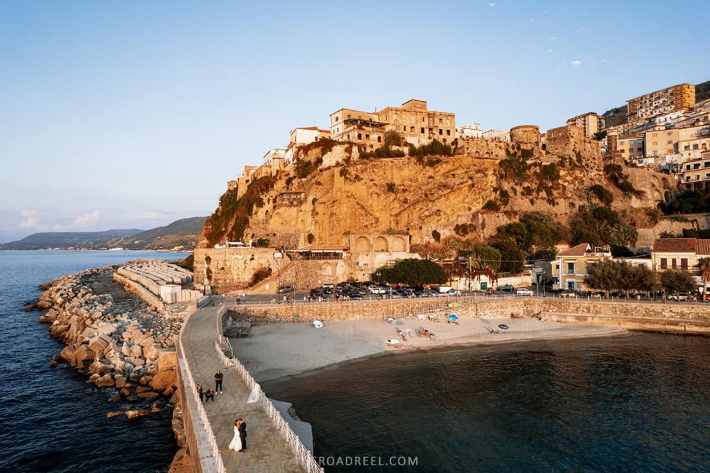 pizzo coastal town in calabria at sunset, pizzo beach and the buildings on the rock, in the foreground a new wed couple kissing, image taking with drone